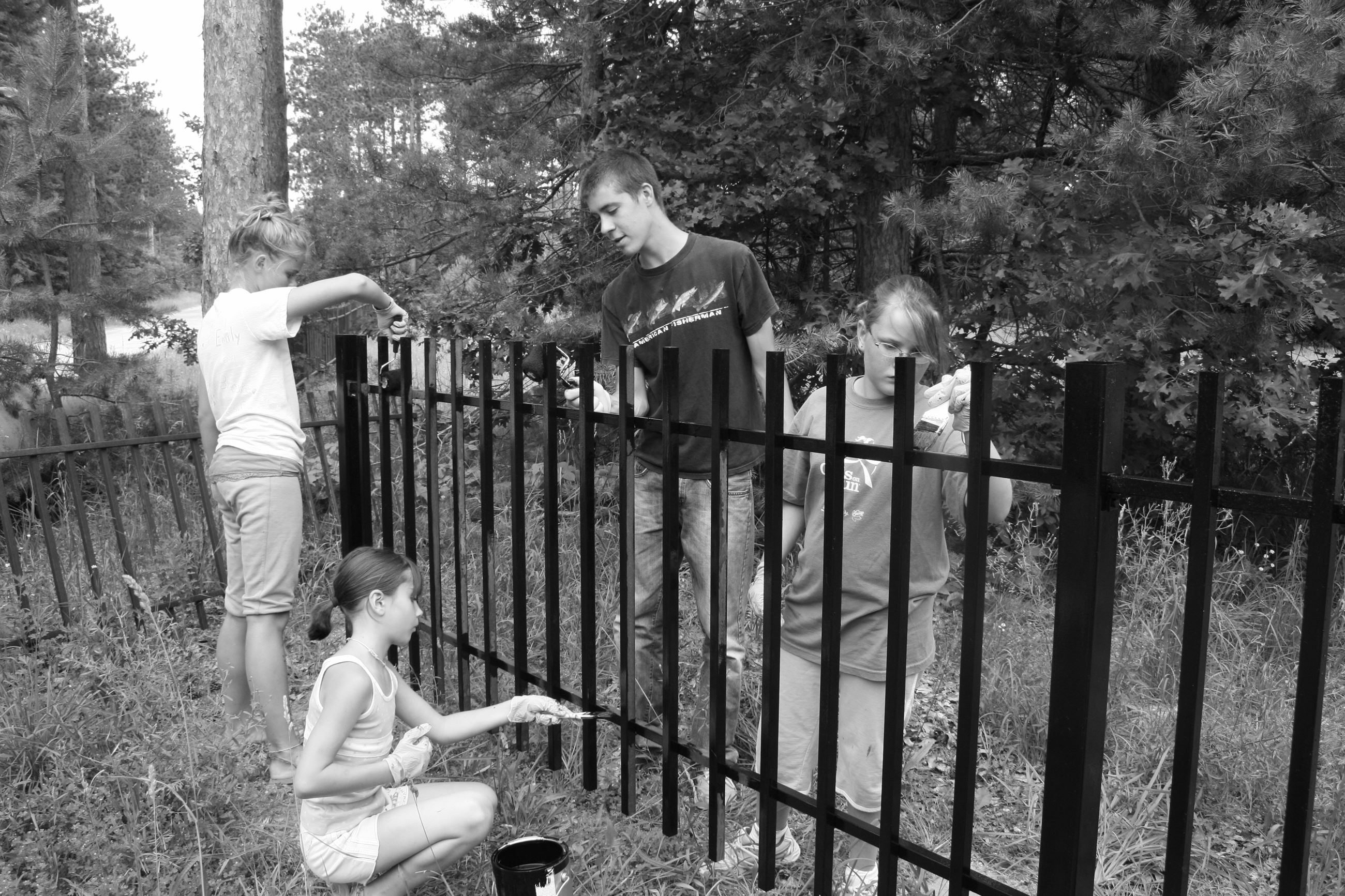 black and white image of kids painting fence
